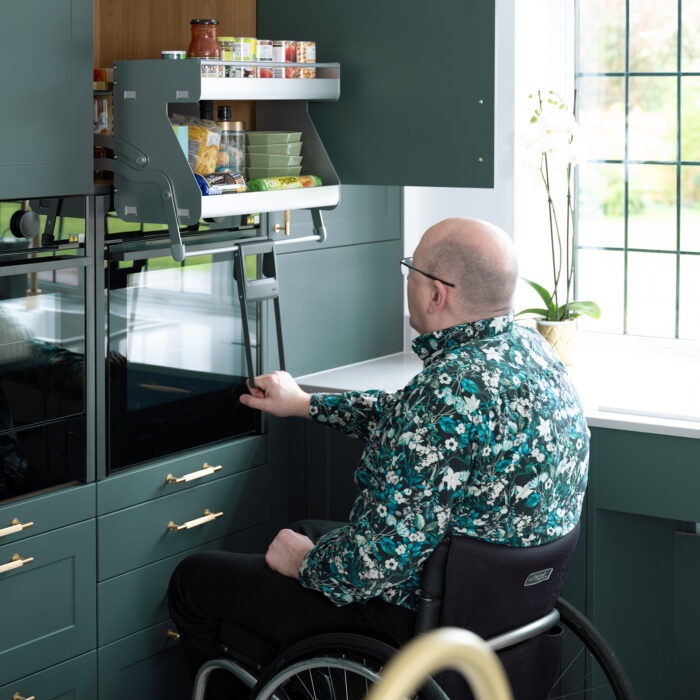 A man in a wheelchair opening a cupboard in a kitchen